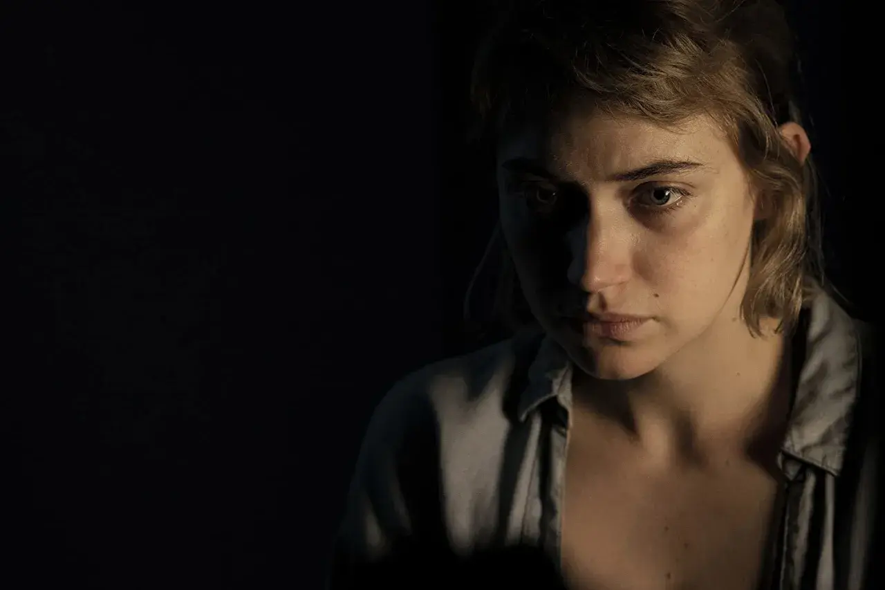Primo piano di una giovane donna con sguardo preoccupato, in penombra. Un'immagine che evoca le atmosfere di "Vivarium", recensione.