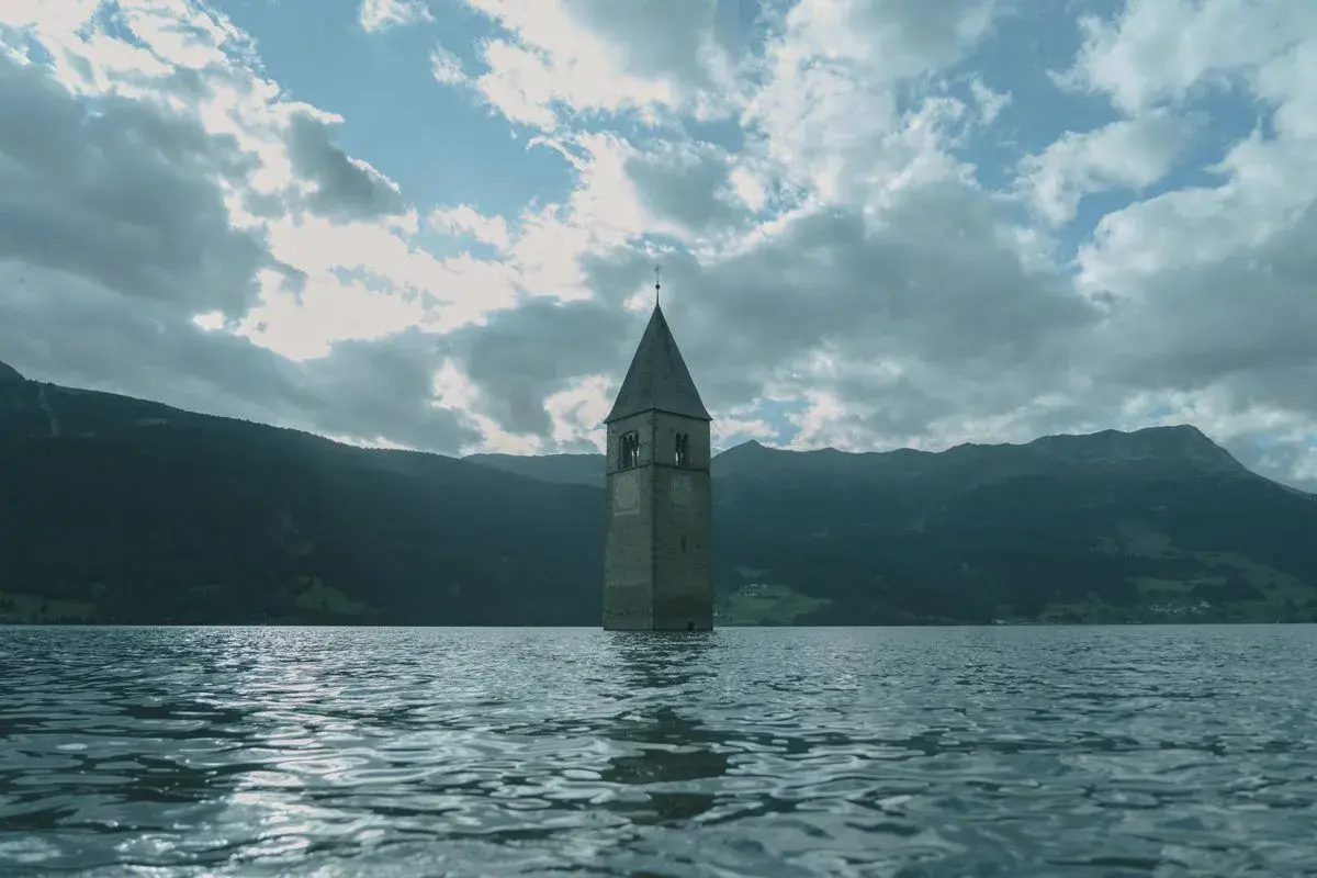 Torre sommersa nel lago, un'icona di Curon. Le recensioni la descrivono come un luogo suggestivo e malinconico, con montagne sullo sfondo.