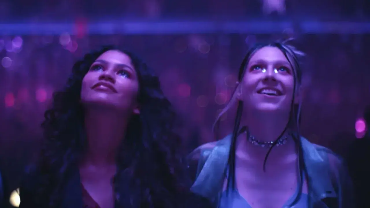 Due ragazze, immerse in luci viola, vivono un momento di pura **euforia 2**.