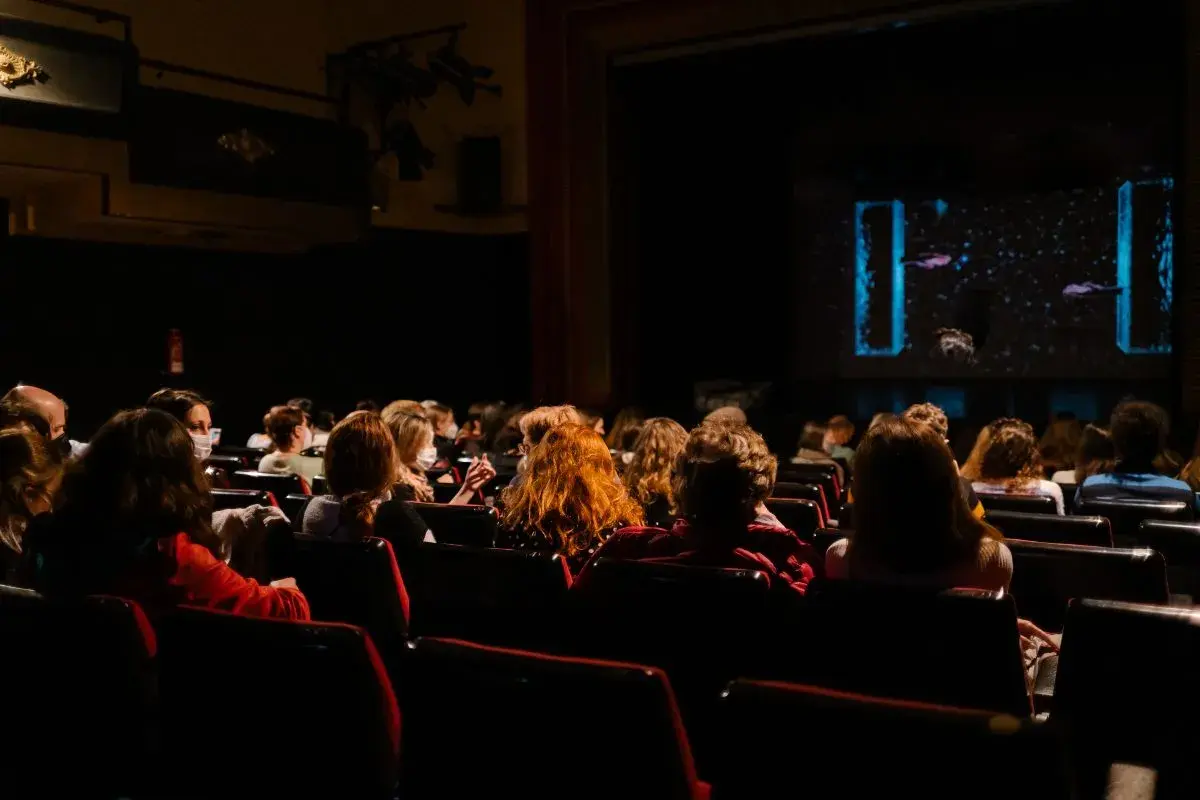 Pubblico in sala, immerso nell'oscurità, attende con il fiato sospeso i monologhi da brividi che stanno per iniziare sul palco illuminato.