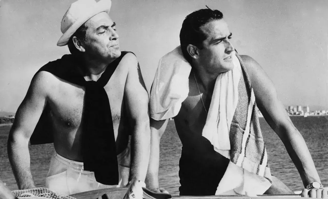 Due uomini su una barca, uno con un berretto da marinaio e una sciarpa, l'altro con un asciugamano. Un'immagine che evoca il significato del sorpasso, film e vita.