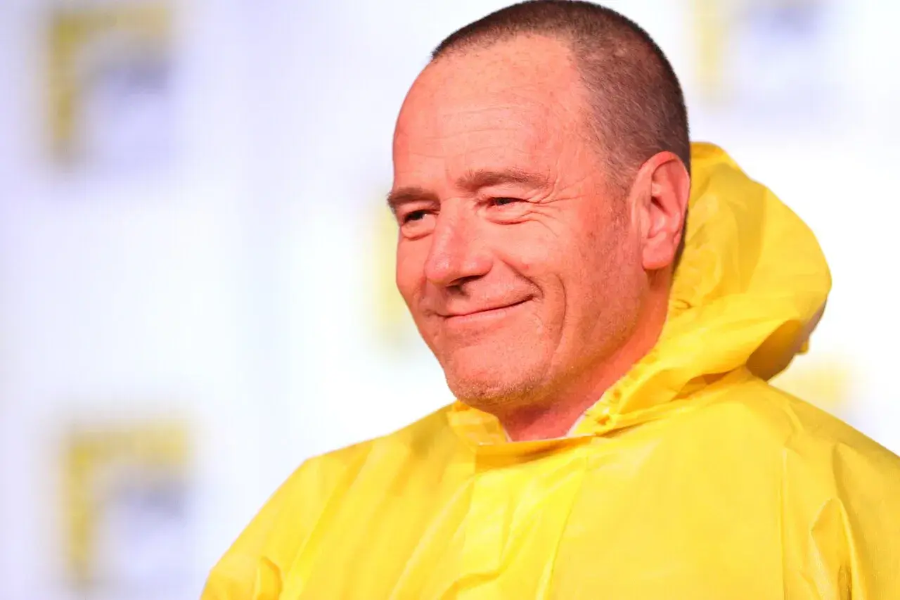 Bryan Cranston sorride con la sua iconica tuta gialla, ricordando le citazioni di Breaking Bad.