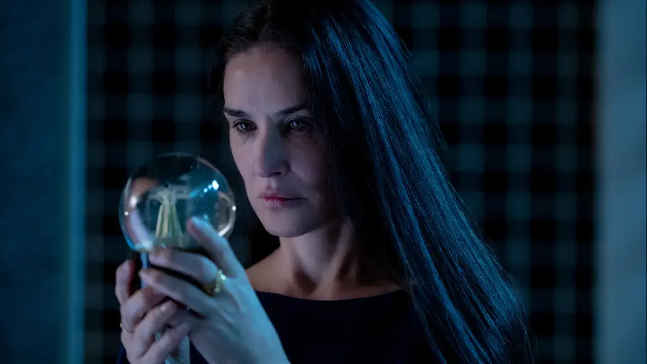 Donna con lunghi capelli scuri osserva una sfera luminosa, un'immagine che evoca mistero e riflessione, come in una recensione di "The Substance".