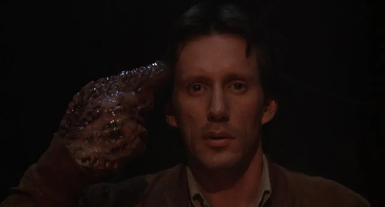 Un uomo con una mano mutata, simile a un tumore, punta alla tempia. Un'immagine disturbante che riflette il videodrome significato.