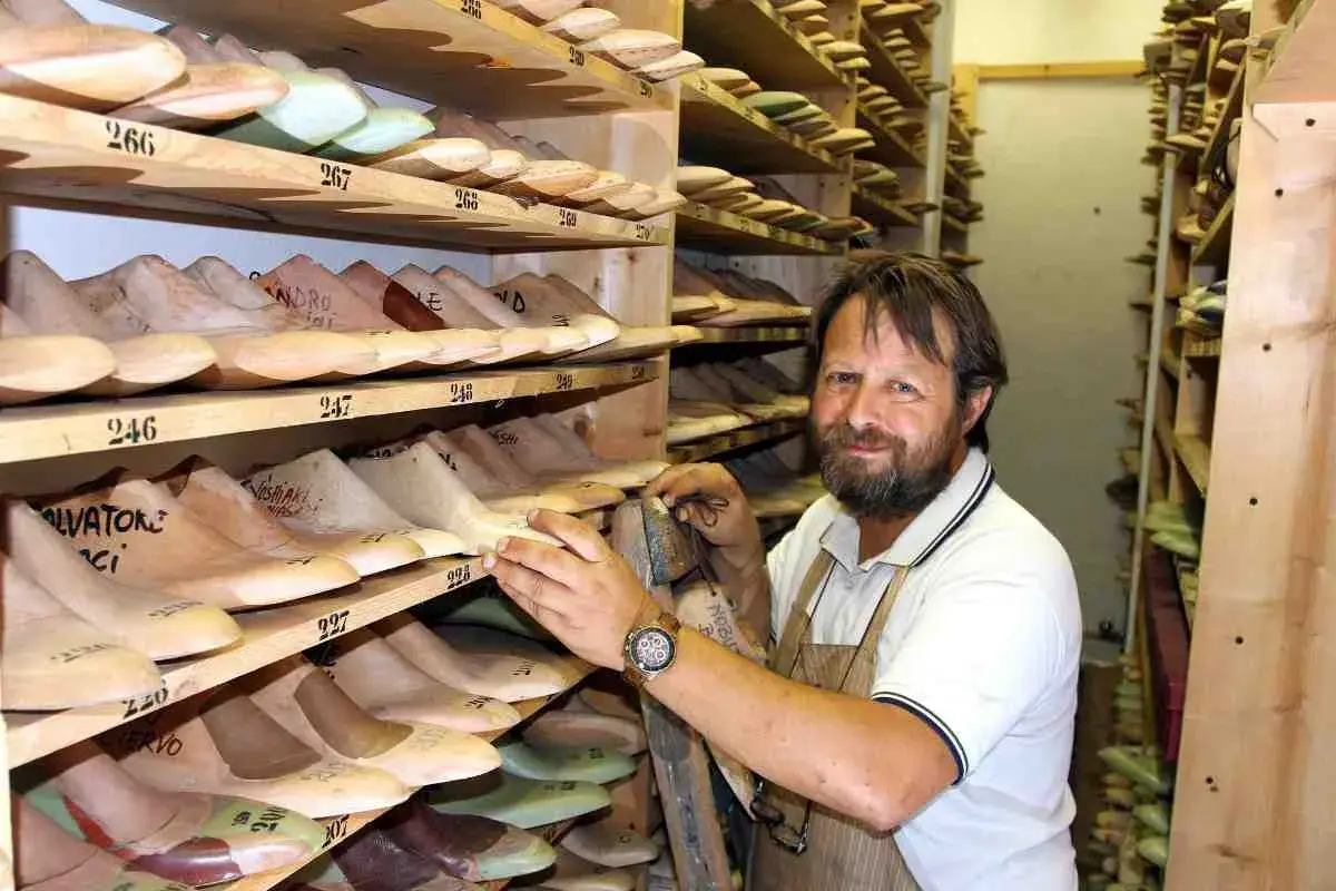 Un calzolaio sorridente in bottega, circondato da forme di legno per scarpe. Sembra Daniel Day Lewis, immerso nel suo mestiere.