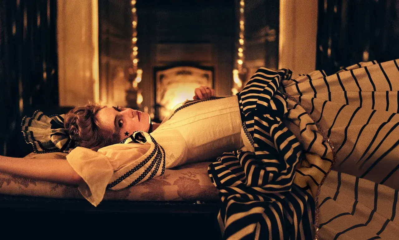La favorita recensione: una donna con un abito a righe giace su un divano, illuminata da luci soffuse.
