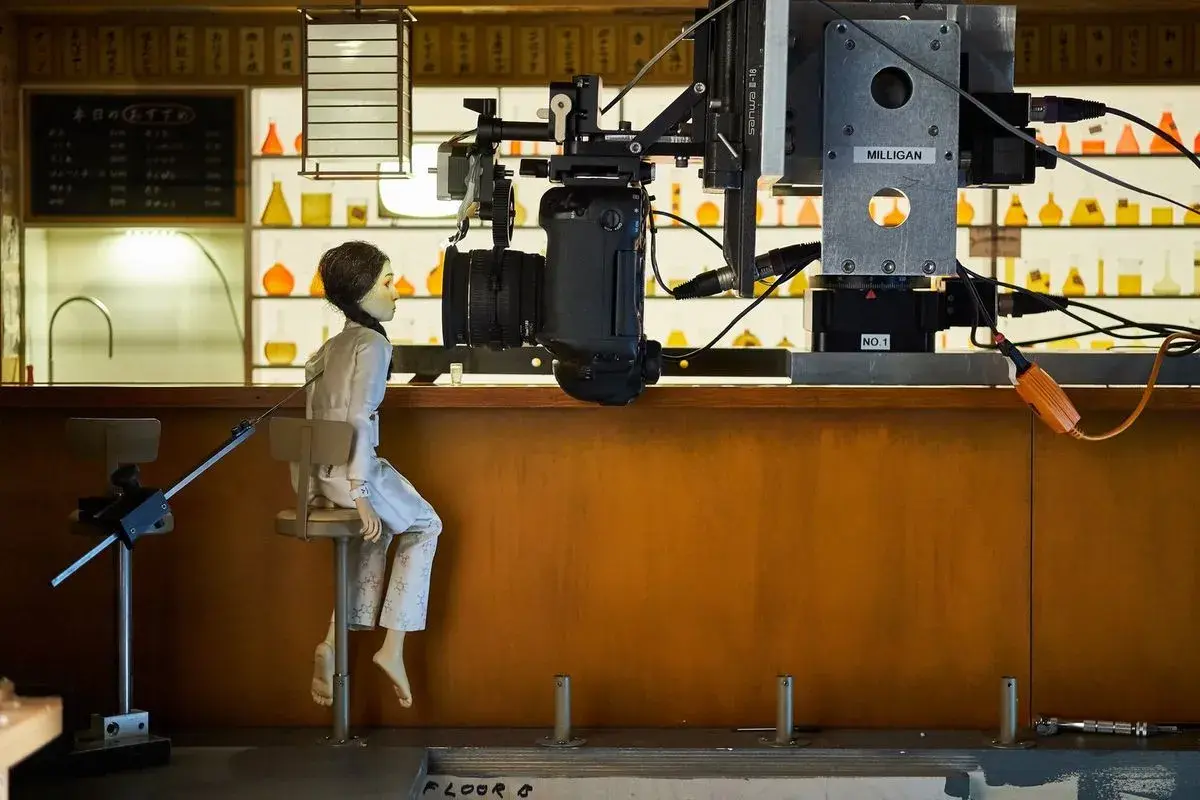 Bambola seduta su uno sgabello, pronta per essere animata in stop motion. La telecamera è posizionata sopra di lei, pronta a catturare ogni movimento.