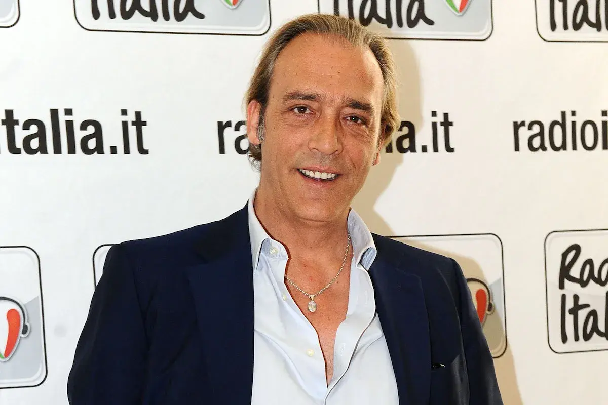 Luca Ward, noto per i suoi ruoli in film e programmi TV, sorride davanti a uno sfondo con il logo di Radio Italia.