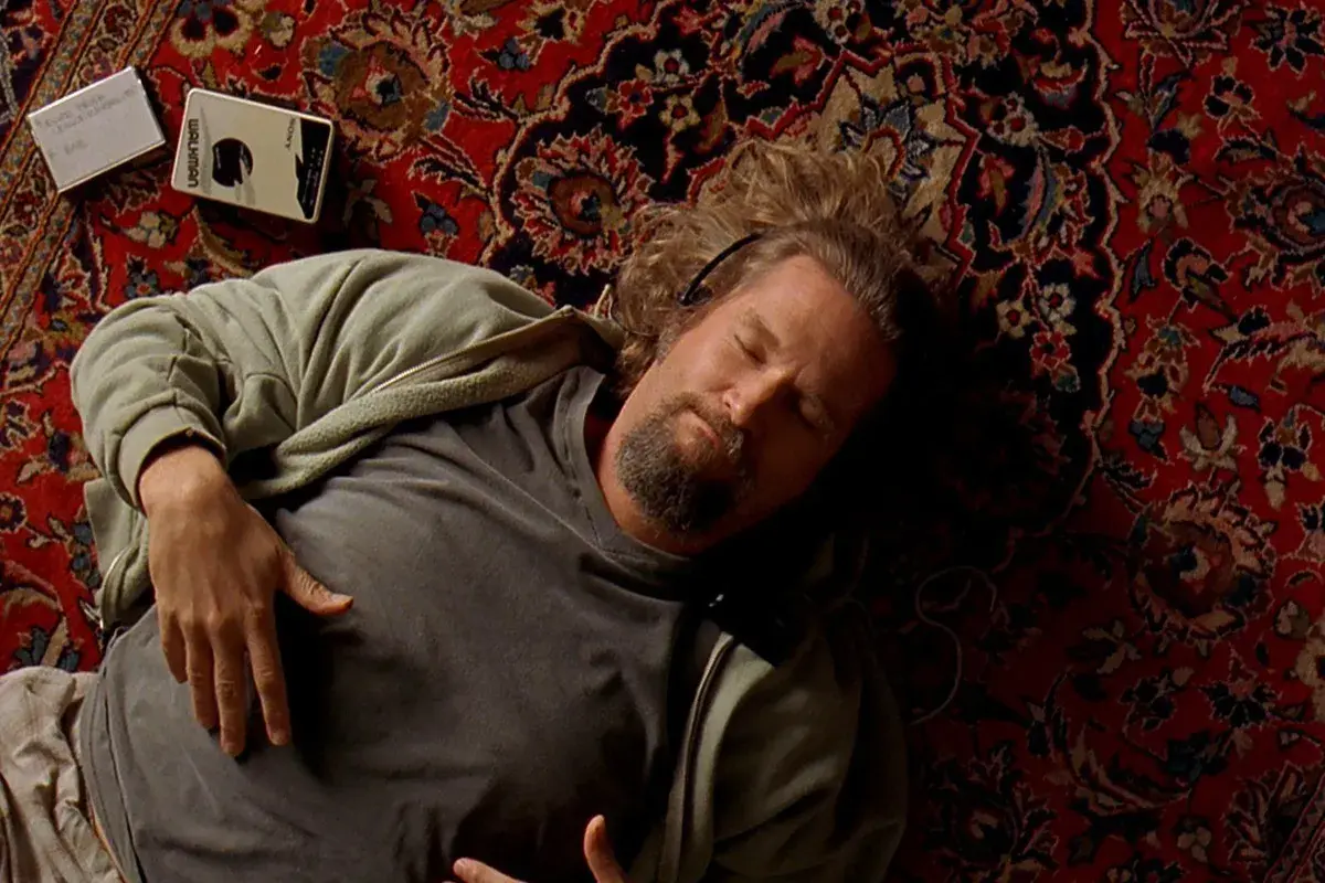 Un uomo con cuffie dorme su un tappeto persiano, accanto a un Walkman. Un'immagine iconica che evoca le recensioni de "Il Grande Lebowski".
