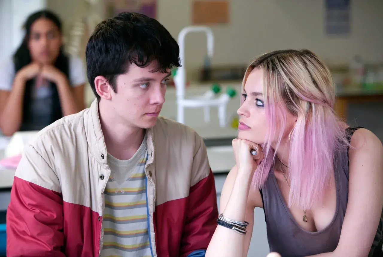 Una recensione di Sex Education: Otis e Maeve si guardano intensamente, mentre un'altra ragazza è sfocata sullo sfondo.
