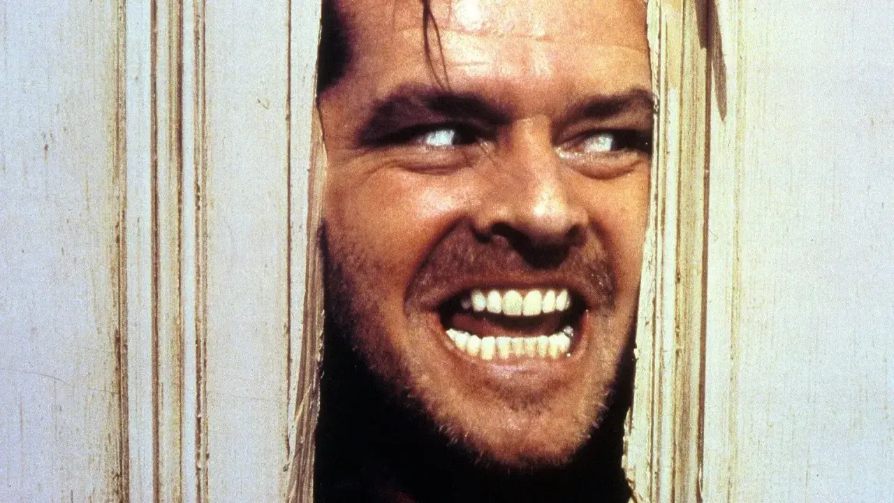 Occhi bianchi e un sorriso folle, un volto che spunta da una porta in un momento di terrore shining congelato.