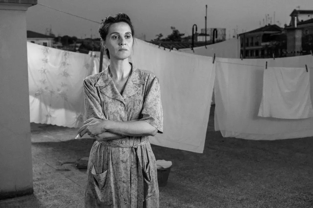 Una donna con un vestito a fiori fuma sul tetto, con panni stesi sullo sfondo. Le recensioni di "C'è ancora domani" lodano la sua interpretazione.