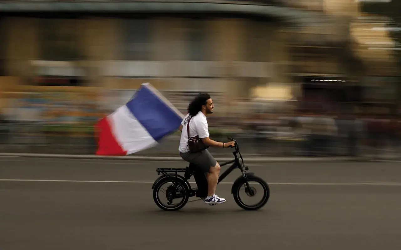 Uomo in bici sfreccia con bandiera francese, un'immagine che sfugge alle recensioni sull'odio.