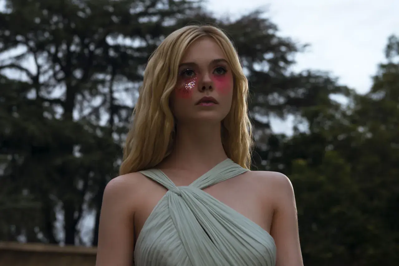 Ragazza con trucco glitterato e vestito verde pallido, un'immagine che evoca il significato di "The Neon Demon" e la sua ossessione per la bellezza.