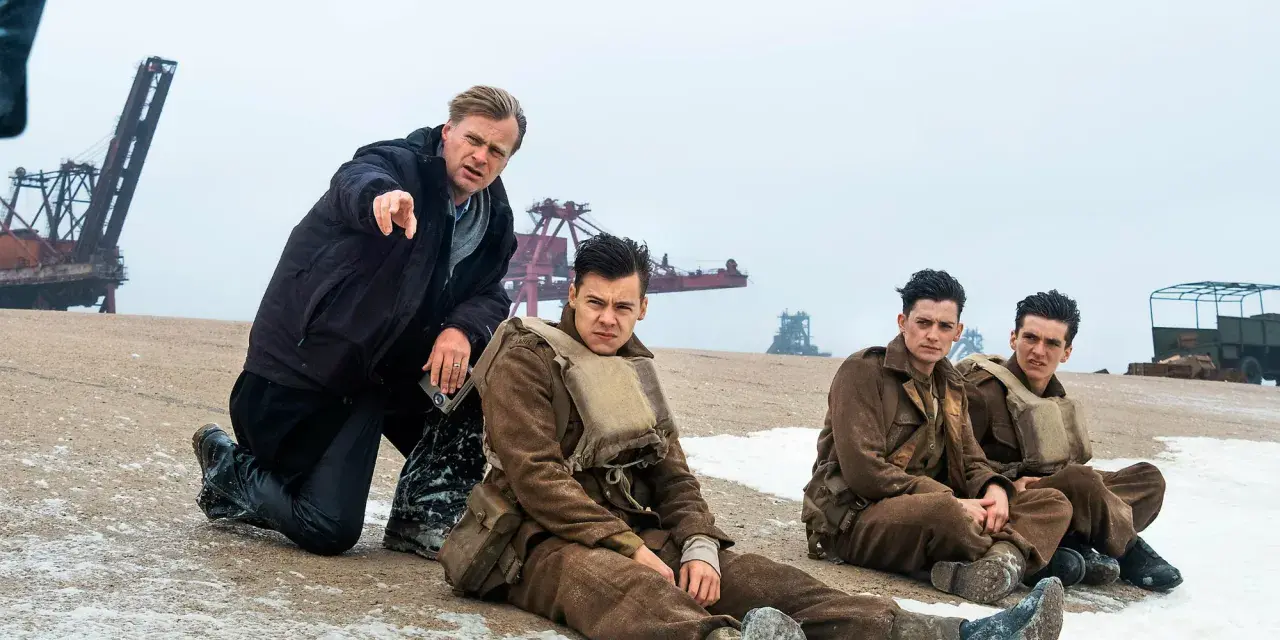 Il cast di Dunkirk, con Christopher Nolan che dirige i giovani soldati seduti sulla spiaggia.