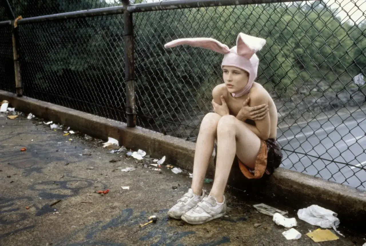 Ragazzo con cappello da coniglio seduto su un muretto, circondato da rifiuti. Un'immagine che evoca la desolazione della trama di Gummo.