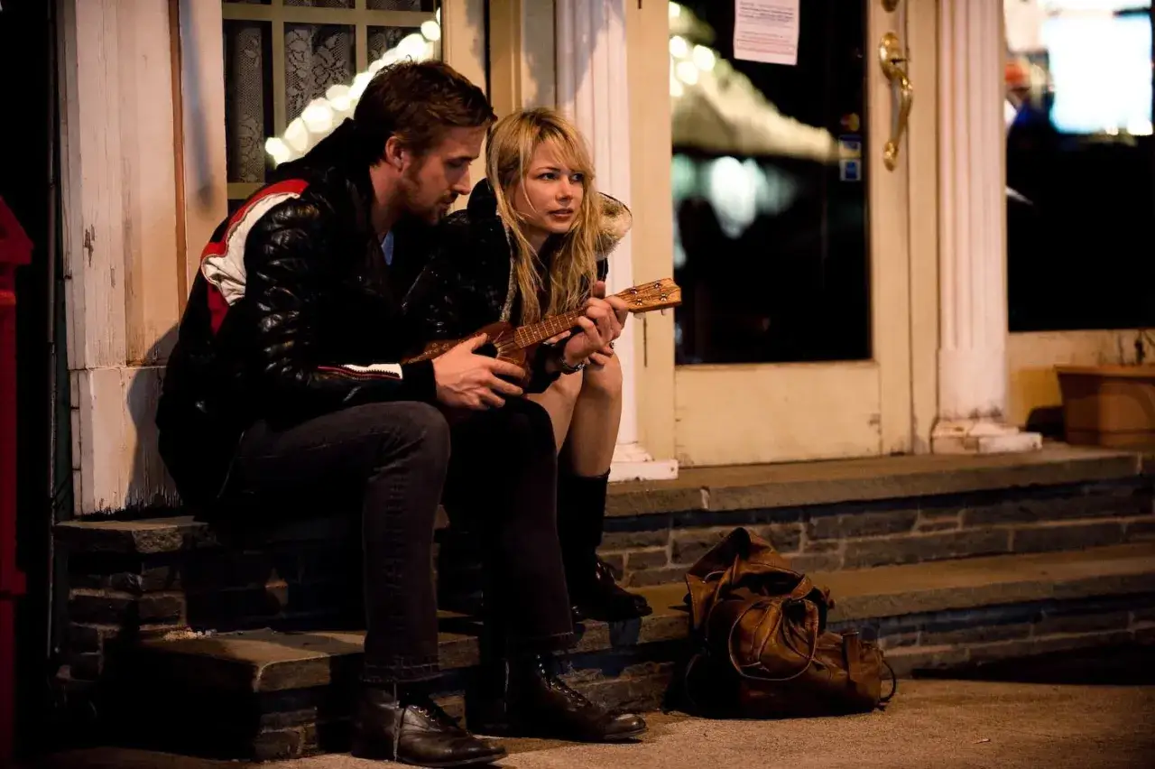 Una coppia seduta sui gradini di casa, lui suona l'ukulele. Scena che anticipa la blue valentine trama e le sue sfumature emotive.