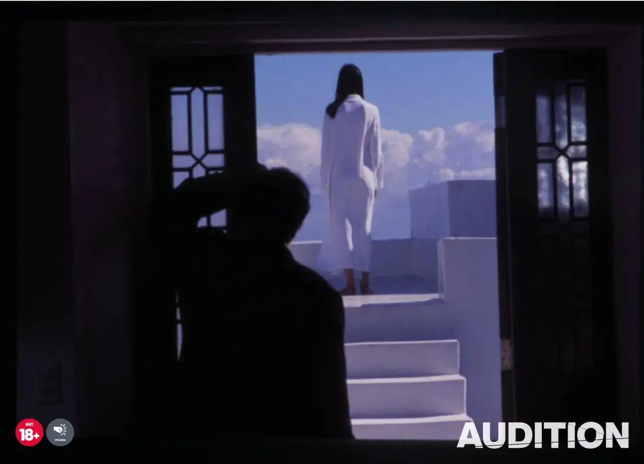 Una donna in bianco attende in cima a una scalinata, sotto un cielo azzurro. Un uomo in ombra la osserva, in un'atmosfera che suggerisce un'audition spiegazione.