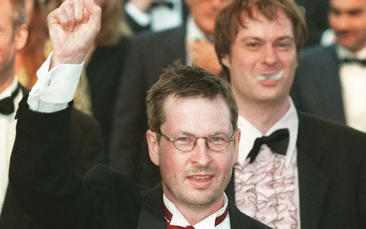 Lars von Trier, regista, alza il pugno in segno di vittoria, circondato da festeggiamenti.