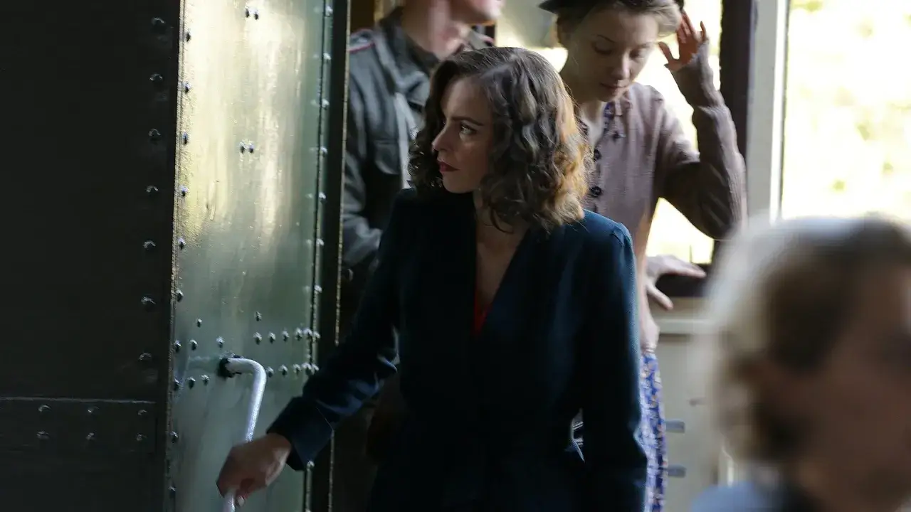 Donna con sguardo intenso, forse custodisce il segreto del suo volto trama. Dietro, figure sfocate in un vagone.