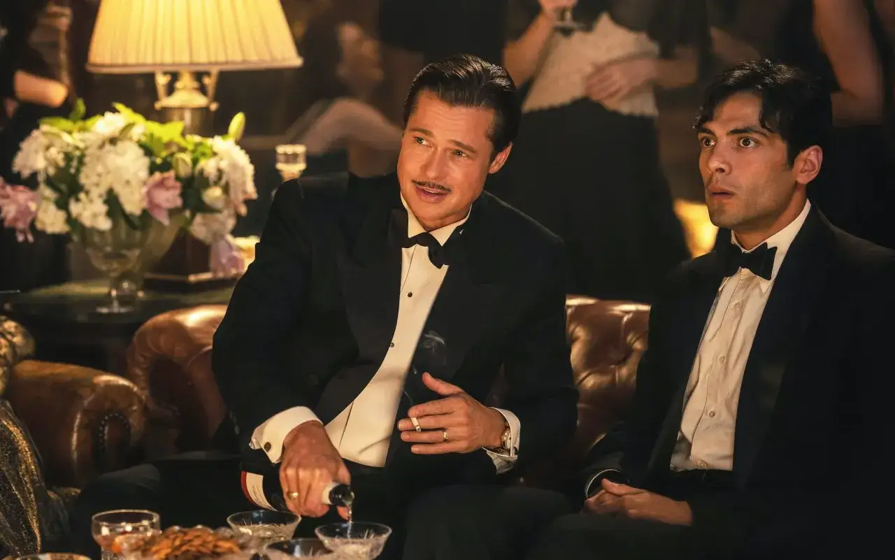 Brad Pitt e Diego Calva, parte del cast di Babylon, brindano con sigaretta e champagne in un'atmosfera festosa.