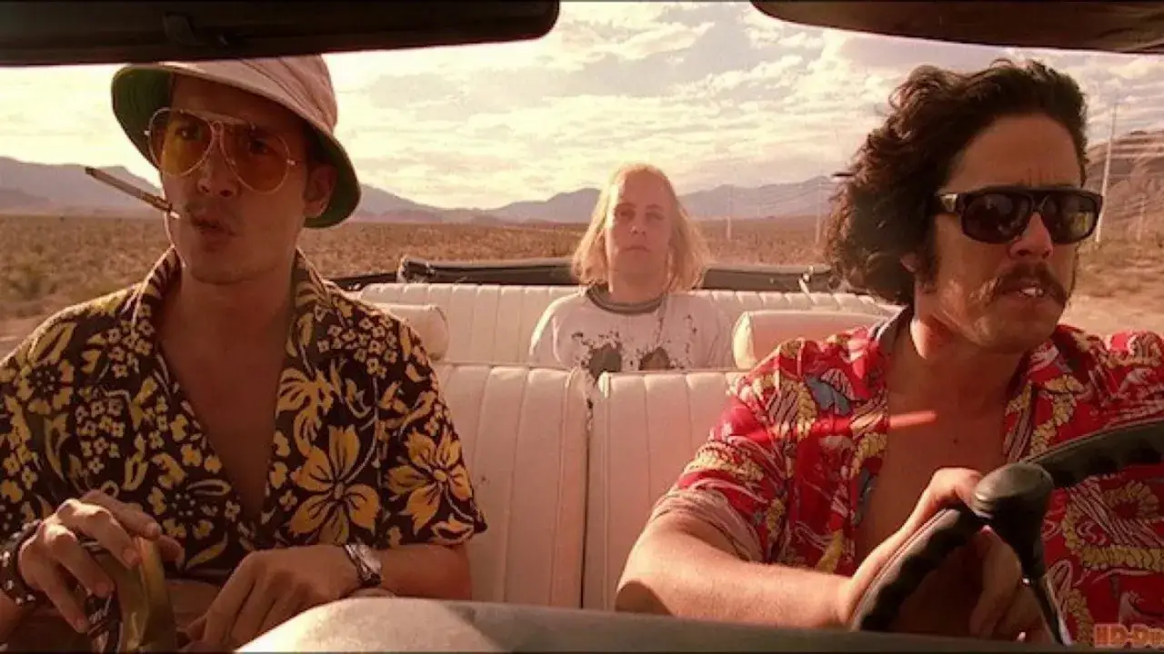 Paura e delirio a Las Vegas: tre uomini in auto nel deserto, uno con sigaretta e occhiali da sole, un altro con baffi e occhiali scuri, e uno al centro con capelli lunghi.