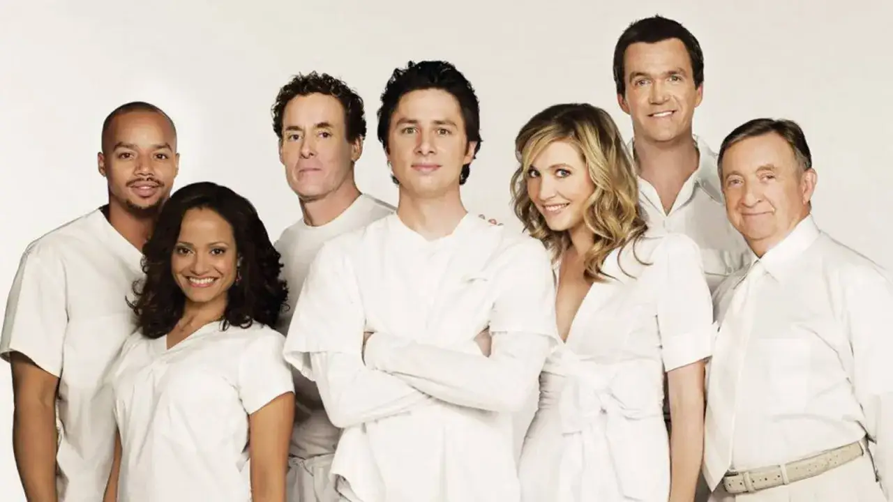 Il cast di Scrubs, medici ai primi ferri, posa sorridendo in camici bianchi.