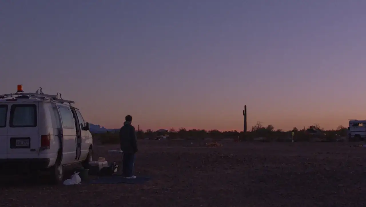 Al tramonto nel deserto, un nomade contempla il suo furgone, un'immagine che evoca la recensione di Nomadland.