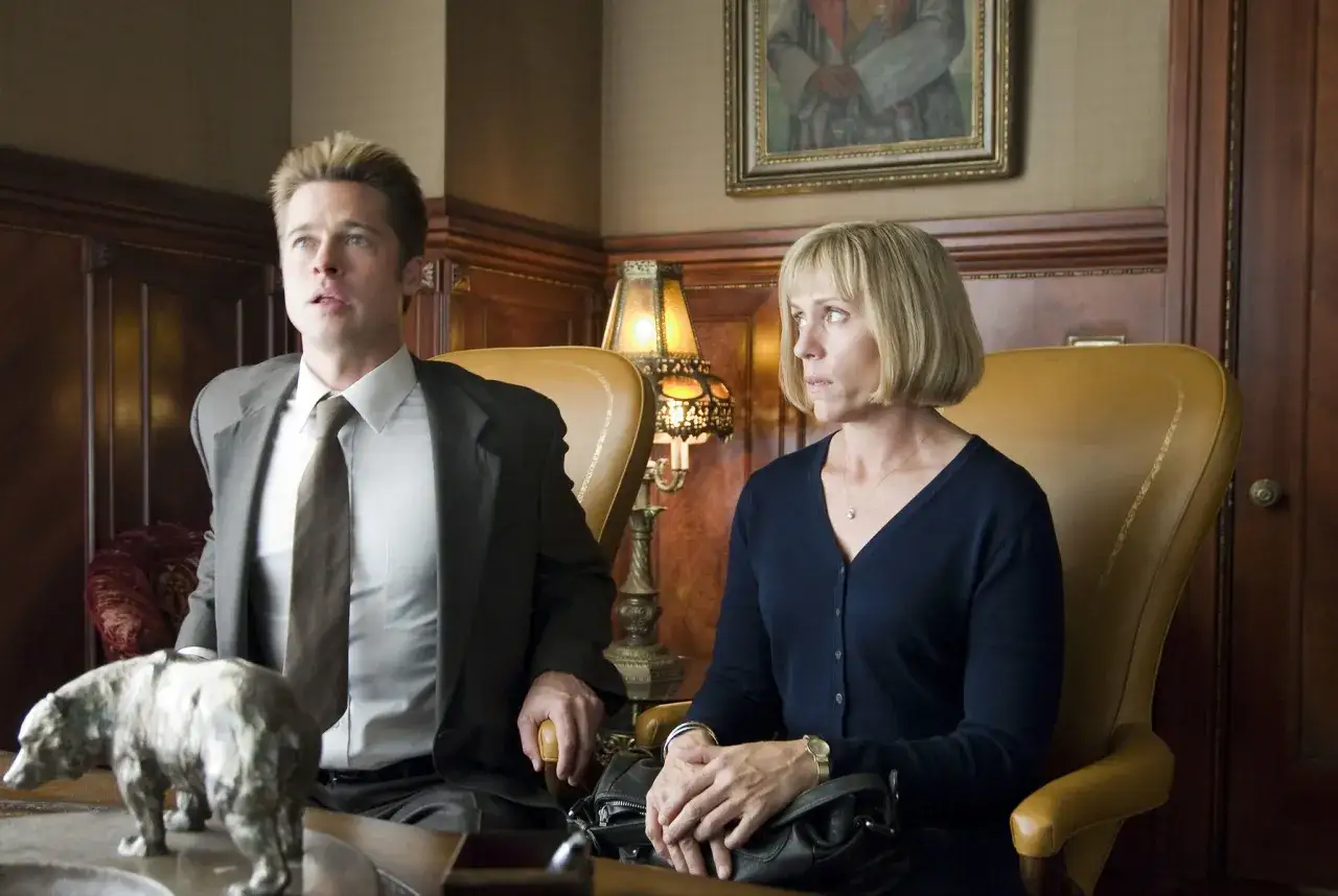 Brad Pitt e Kristen Wiig nel cast di Burn After Reading - a prova di spia, seduti in poltrone, con una statuetta di orso.
