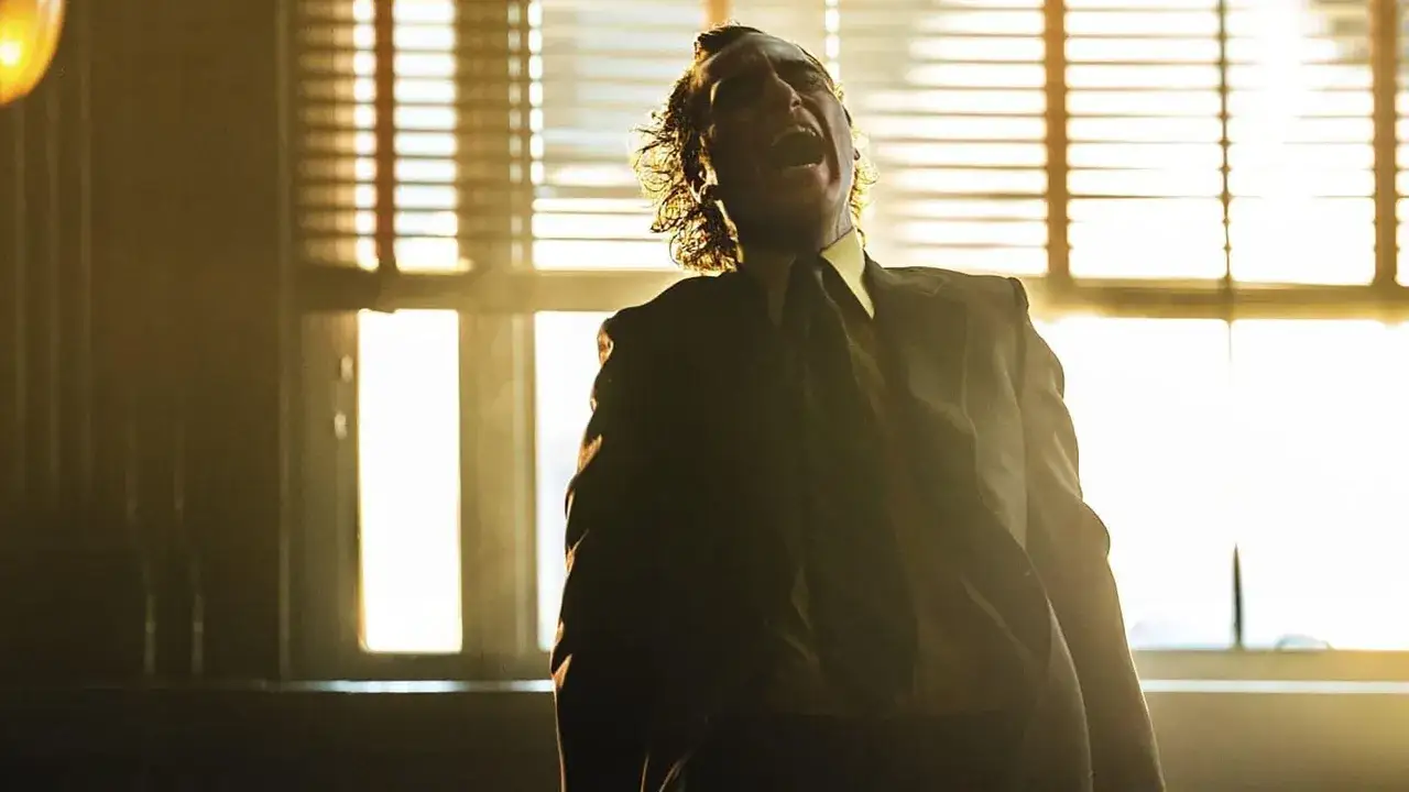 Arthur Fleck, nel joker scena finale, urla liberato, con i capelli scuri che gli ricadono sul viso illuminato da una luce dorata.