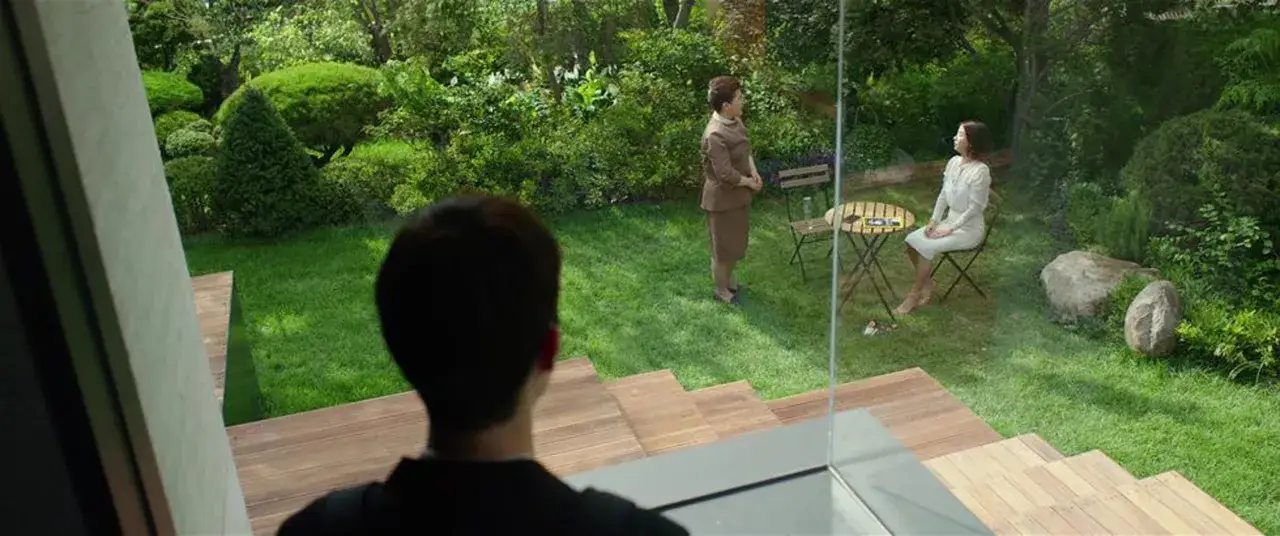 Giardino lussureggiante, due donne conversano. Una scena che fa riflettere sulla recensione di Parasite.