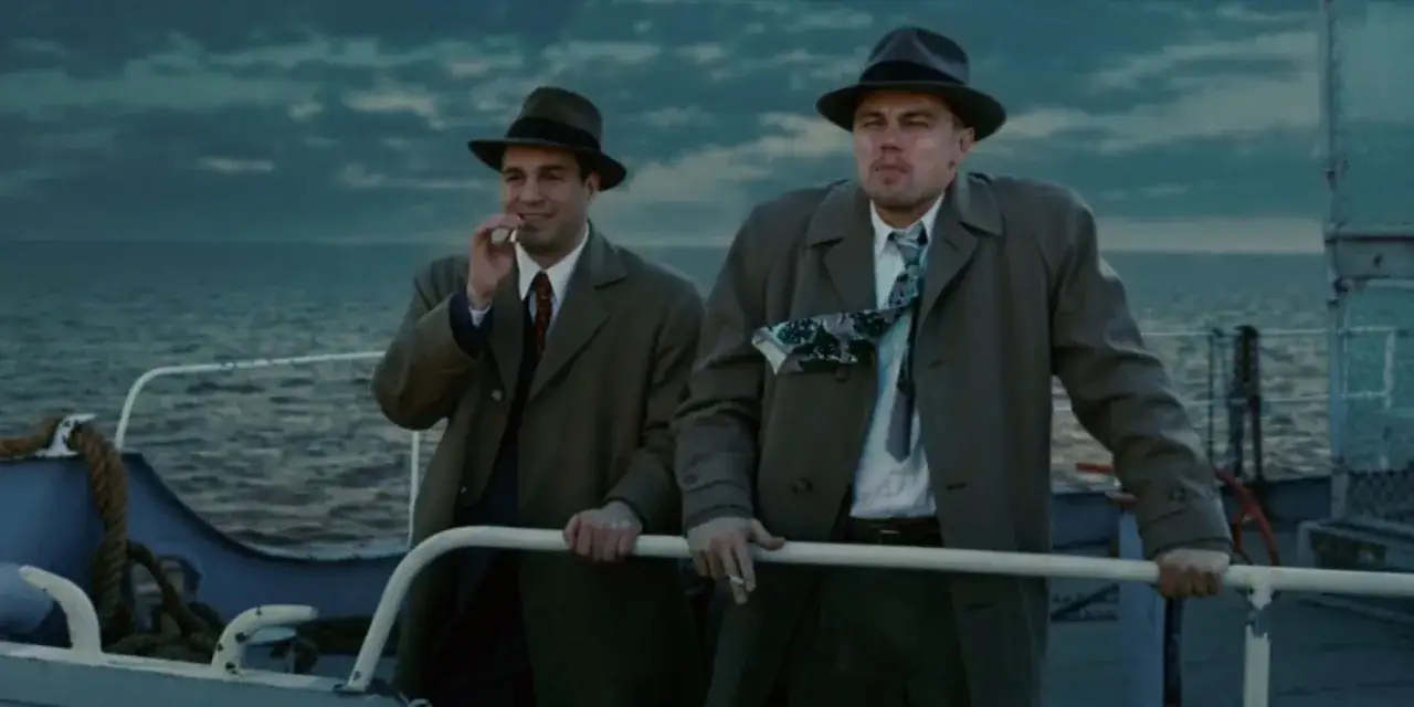 Due uomini in cappello e soprabito fumano su una barca, in una scena che ricorda i premi di Shutter Island.