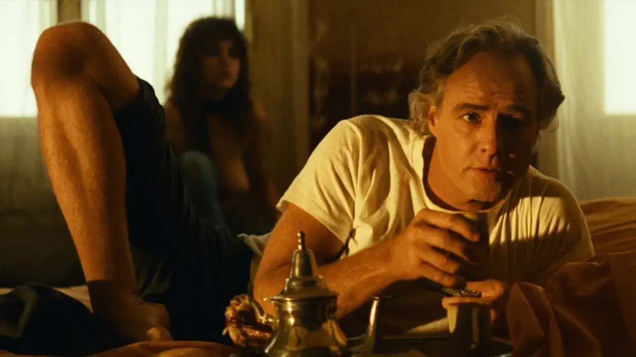 Ultimo tango a Parigi: Marlon Brando, in una scena iconica, tiene una tazza, mentre una donna sfocata è sullo sfondo.
