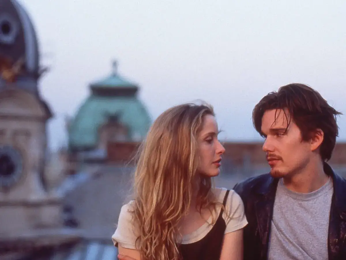 Jesse e Celine si guardano intensamente, sullo sfondo di tetti parigini. Un momento iconico della before midnight trilogia.
