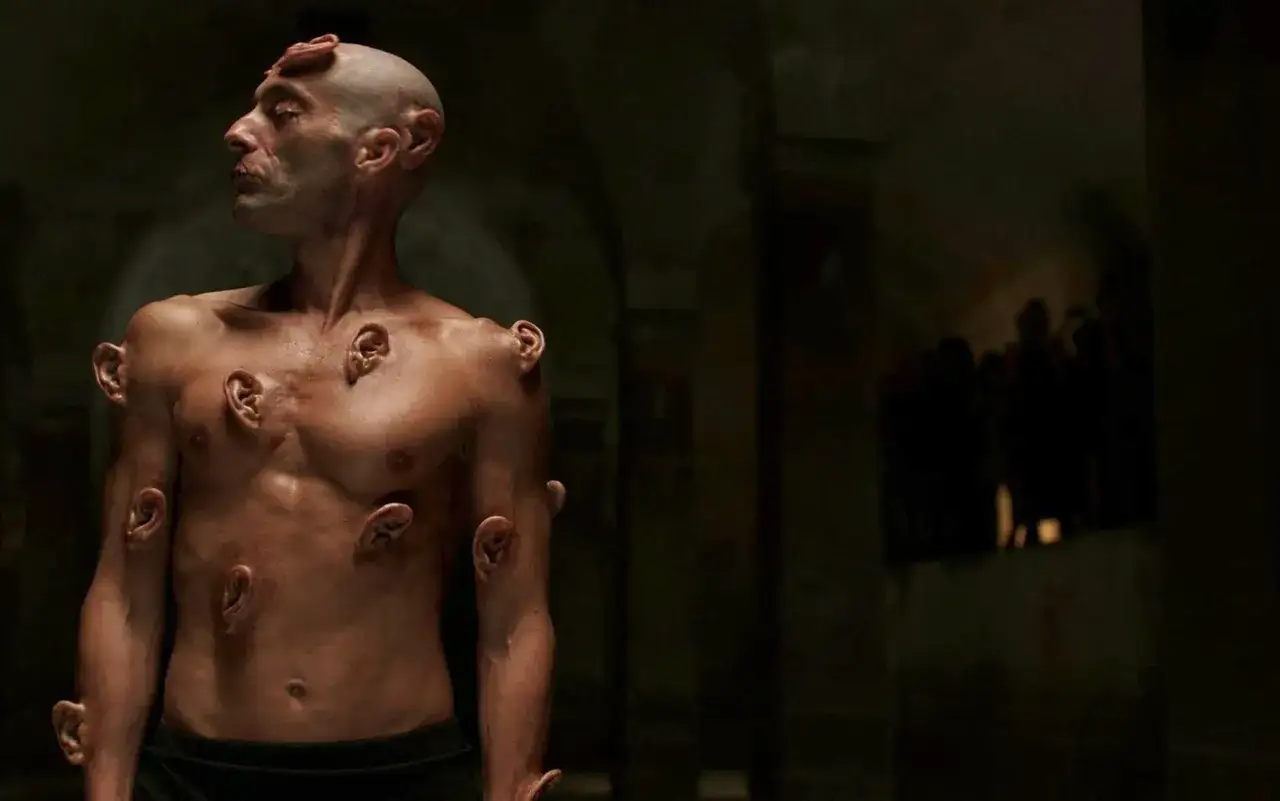Uomo con orecchie innestate sul corpo, un'immagine che evoca il videodrome significato di trasformazione e ossessione mediatica.
