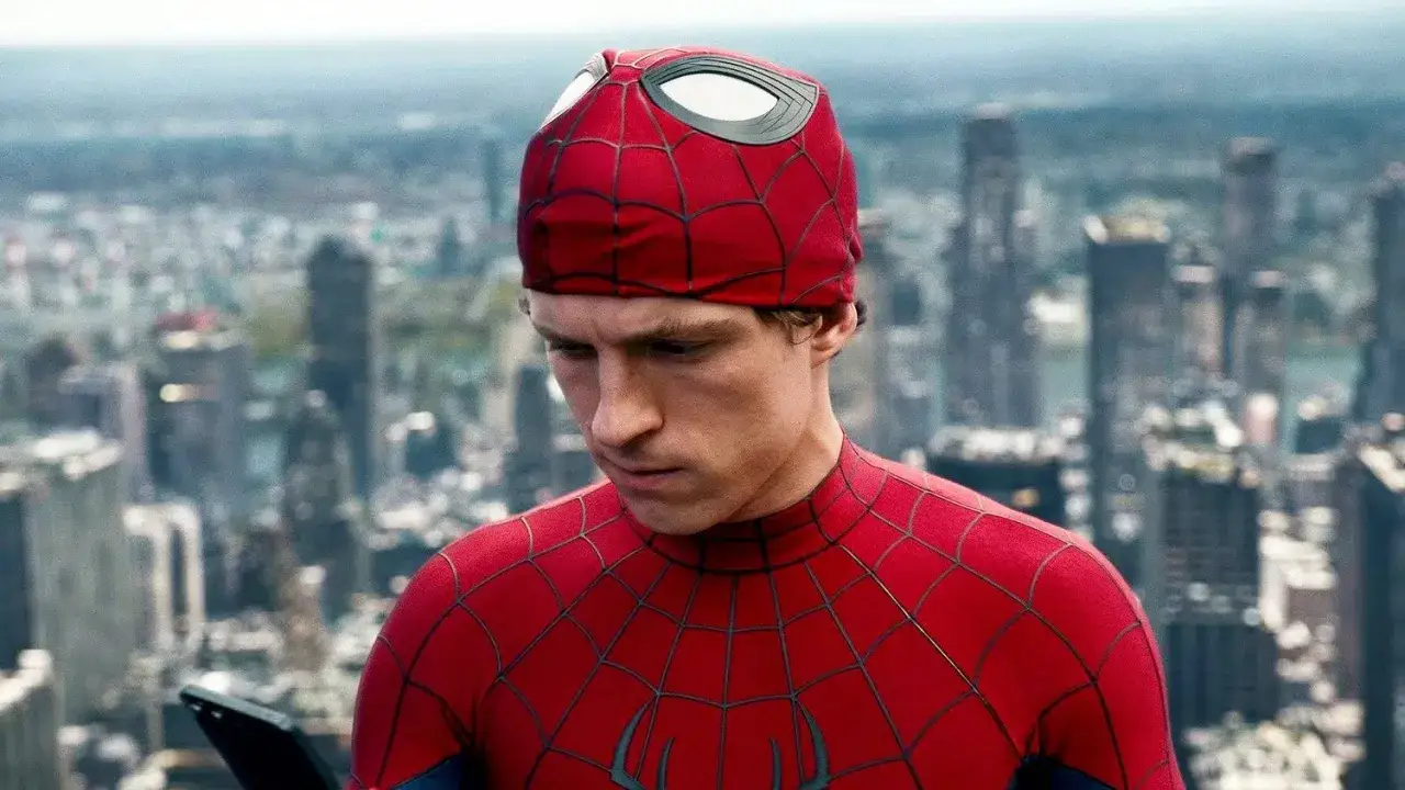 Tom Holland nei panni di Spider-Man, con il costume rosso e blu, guarda un tablet sullo sfondo di una città. La sua maschera è leggermente sollevata. Una recensione di Spider-Man.