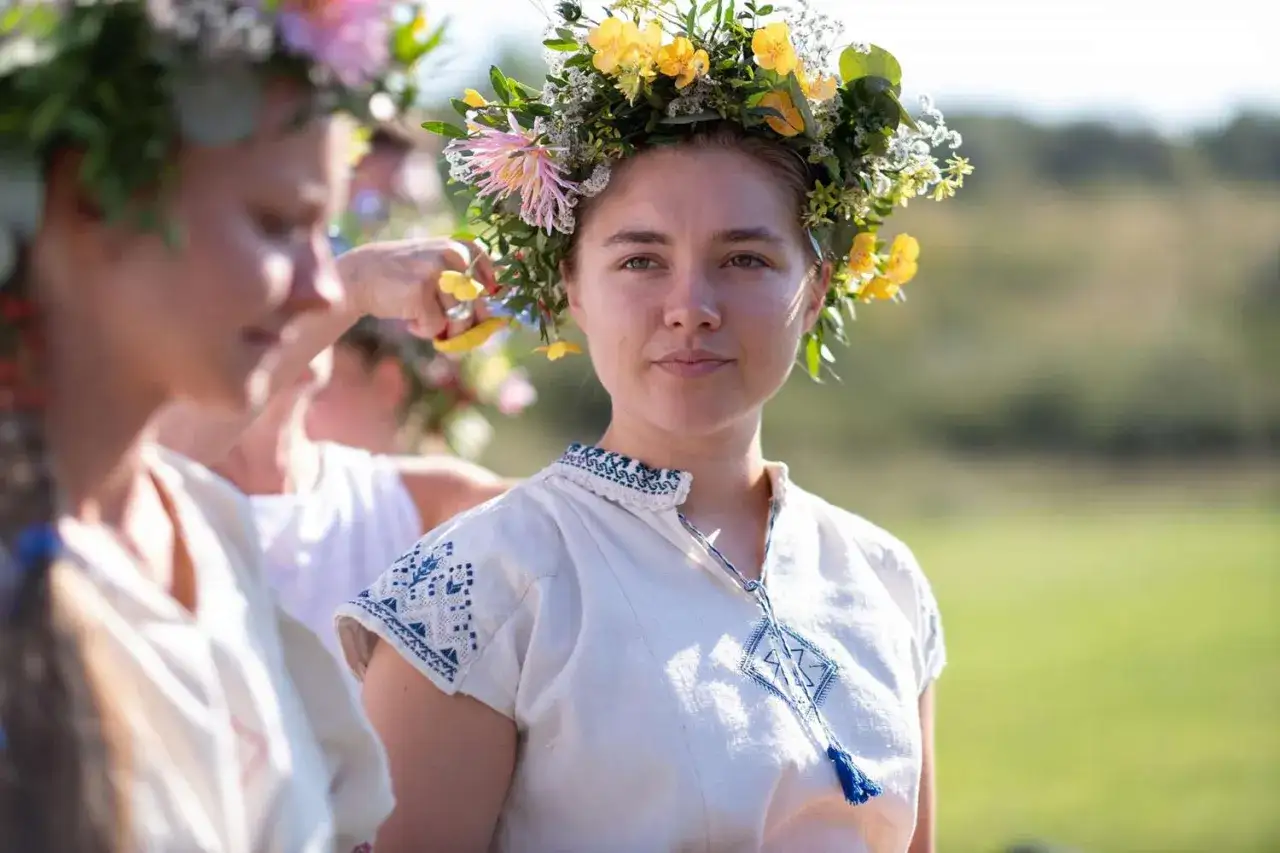 Una donna con una corona di fiori gialli e rosa, vestita con abiti tradizionali ricamati. Un'immagine che evoca l'atmosfera di Midsommar, perfetta per una recensione.