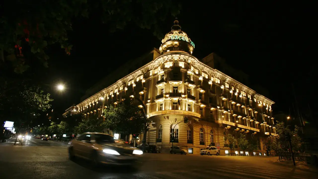 Edificio storico illuminato di notte, un'auto sfocata attraversa la strada. La grande bellezza spiegazione è in questa scena notturna.