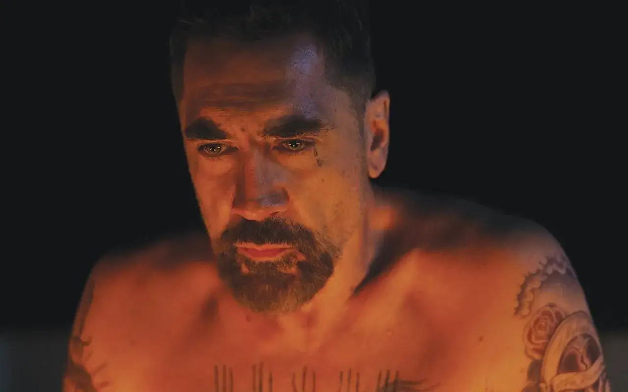 Uomo con tatuaggi e barba, illuminato da una luce calda. Un'immagine che evoca la tensione di una recensione di Cape Fear.