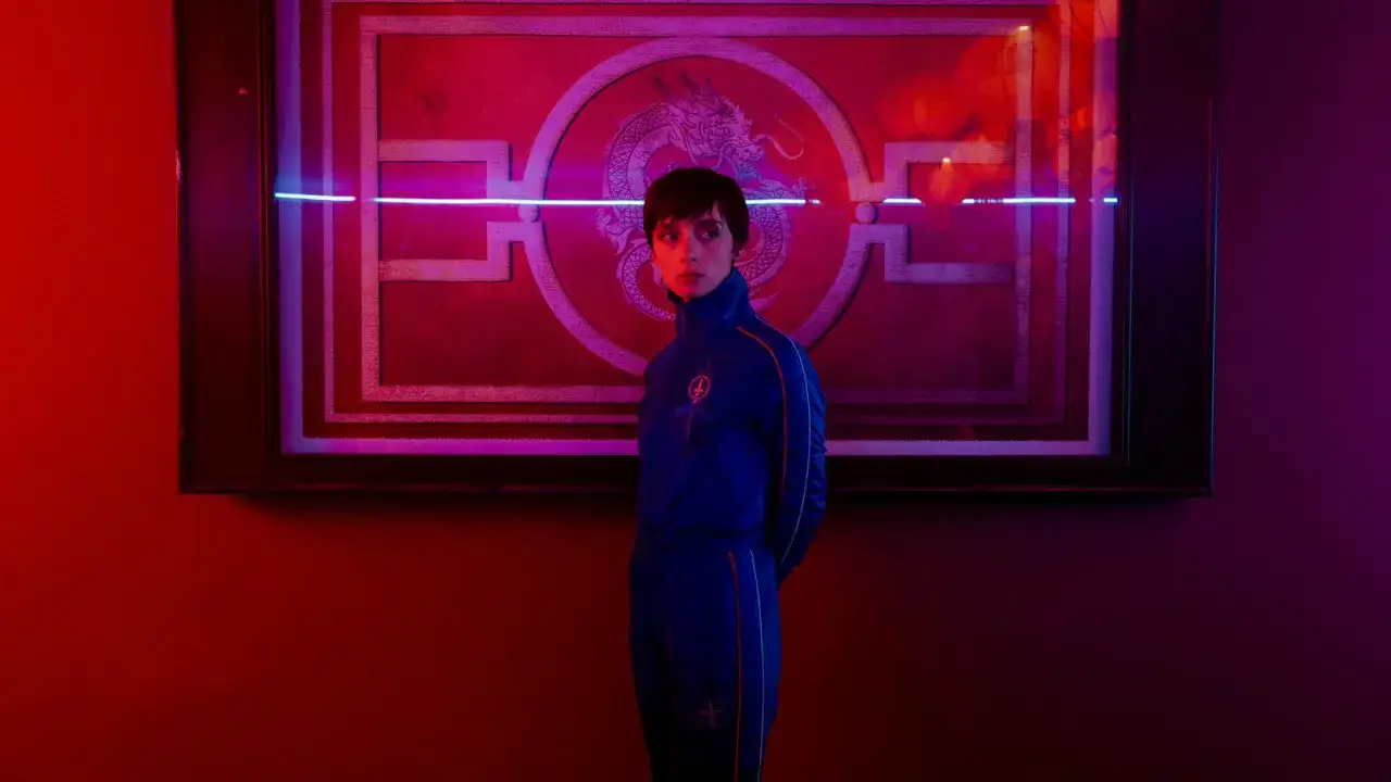 Ragazza in tuta blu davanti a un quadro con drago, in un'atmosfera rossa e blu. Recensione