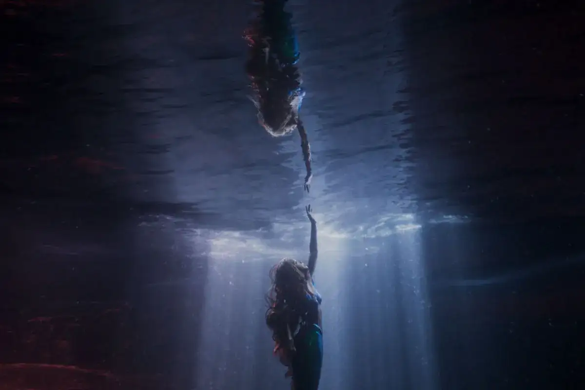 La sirenetta recensioni: due sirene si tendono le mani sotto il mare, raggi di luce filtrano dall'alto.