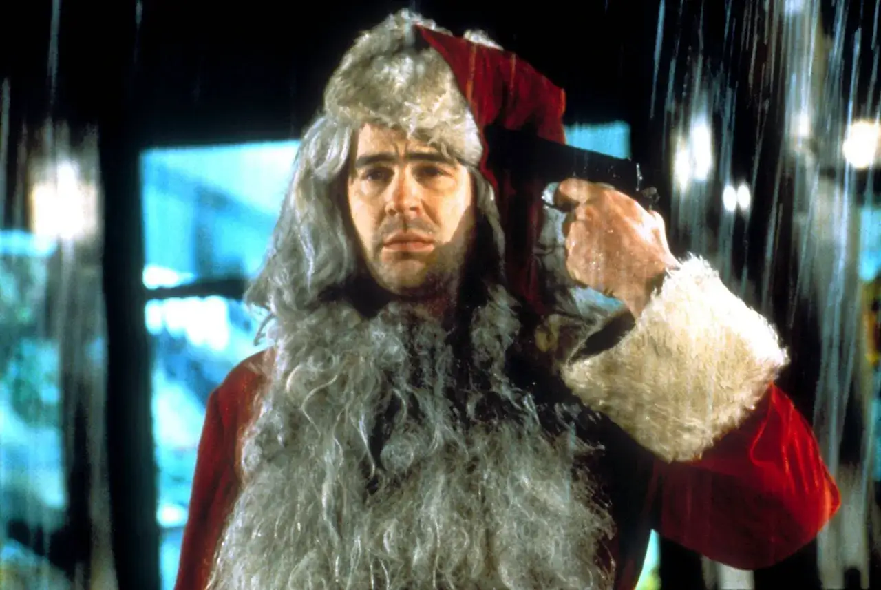 Un uomo con barba e cappello da Babbo Natale tiene una pistola puntata alla tempia. Sembra una scena da