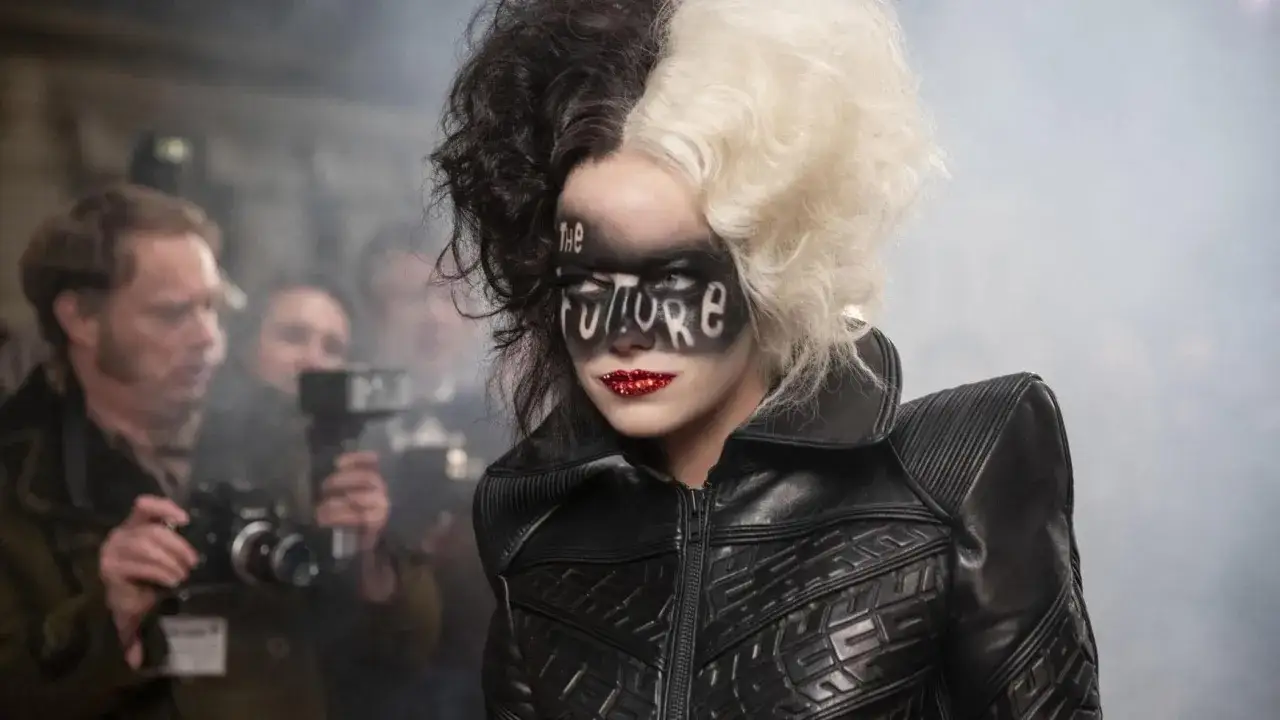 Cruella con trucco audace e capelli bicolore, circondata da fotografi. Le recensioni per questo look sono state un successo.