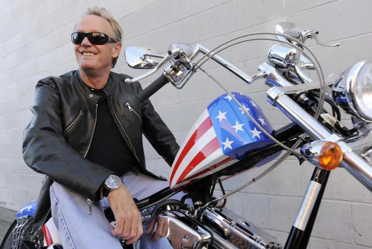 Peter Fonda, icona di Easy Rider, sorride su una moto con serbatoio a stelle e strisce. La sua morte ha lasciato un vuoto.