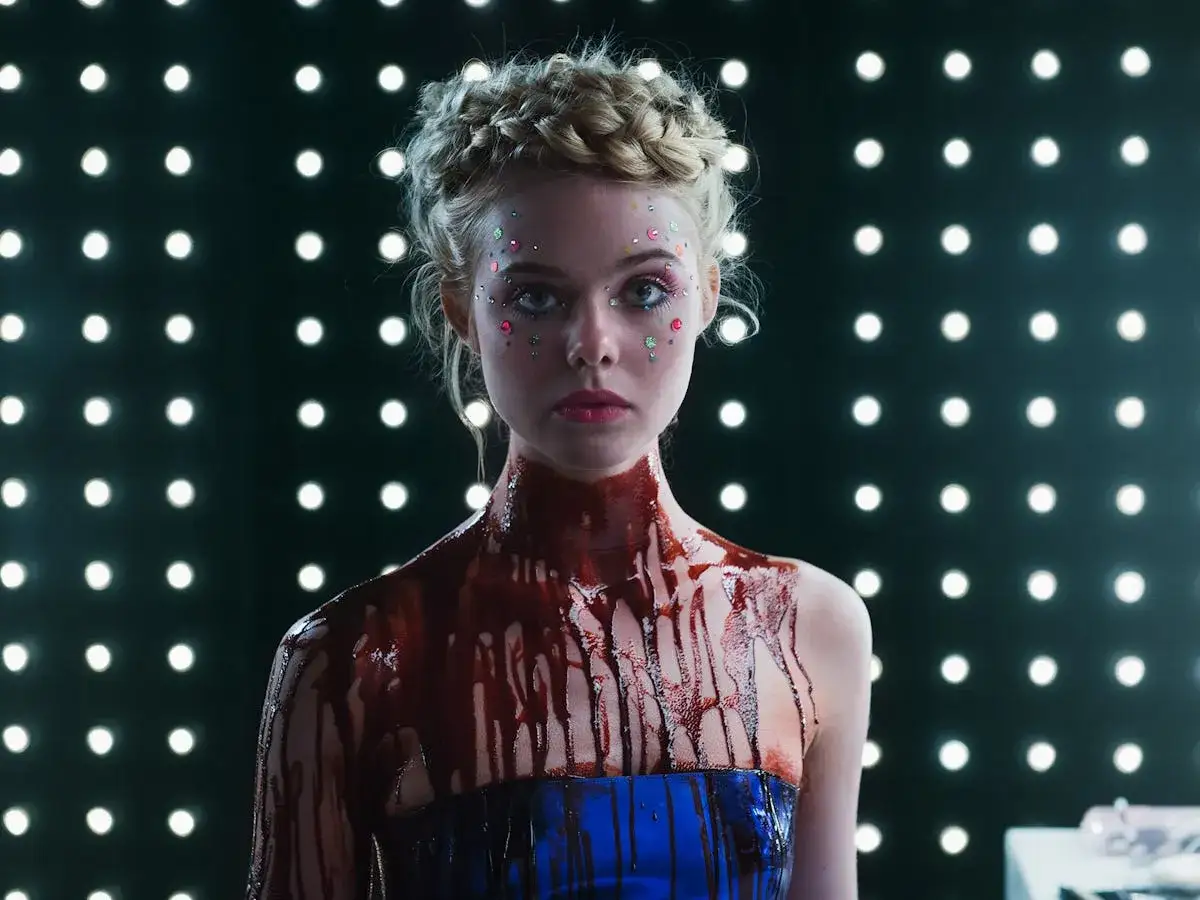 La protagonista di The Neon Demon, con glitter sul viso e un liquido rosso che cola, riflette il suo significato oscuro e la sua ambizione nel mondo della moda.