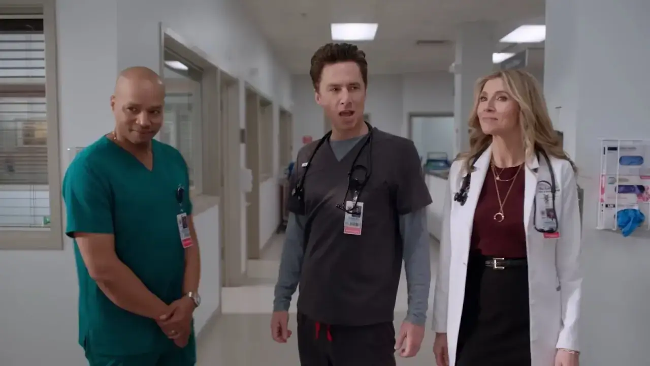 Tre medici in un corridoio ospedaliero, uno in camice verde, uno in scrubs grigi e una dottoressa in camice bianco. Una scena che fa pensare a una scrubs recensione.