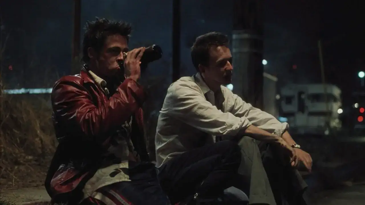 Il narratore di Fight Club, con giacca rossa, beve da una bottiglia. Accanto a lui, un uomo in camicia bianca osserva il buio.